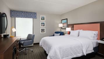 A hotel room with a large bed, a desk with a chair, a television, and framed pictures on the wall.