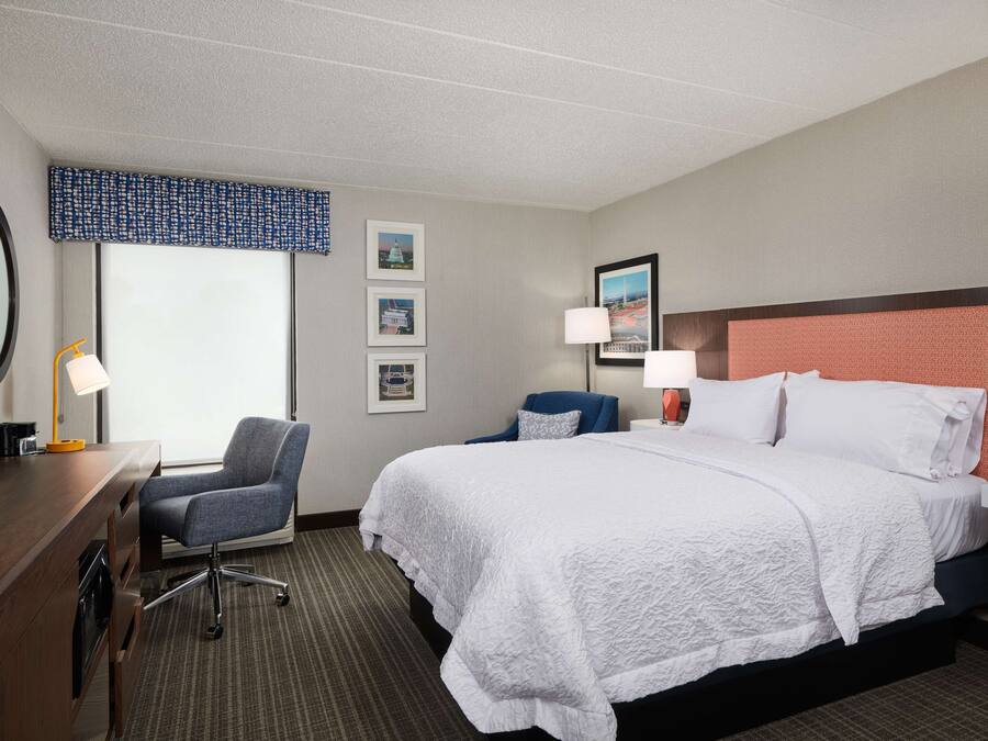 A hotel room with a large bed, a desk with a chair, a television, and framed pictures on the wall.