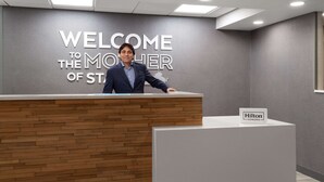 Un mostrador de recepción con un cartel que dice "WELCOME TO THE MOTHER OF STAY", una placa de "Hilton Honors" y una decoración de diseño moderno.