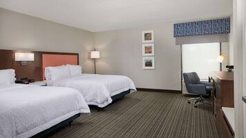A hotel room with two beds, a desk, a chair, a lamp, and artwork on the wall.
