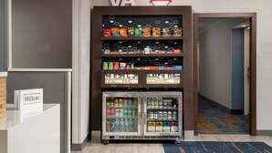 Máquina expendedora con aperitivos y bebidas, un letrero de Hilton Honors e indicaciones de golosinas.