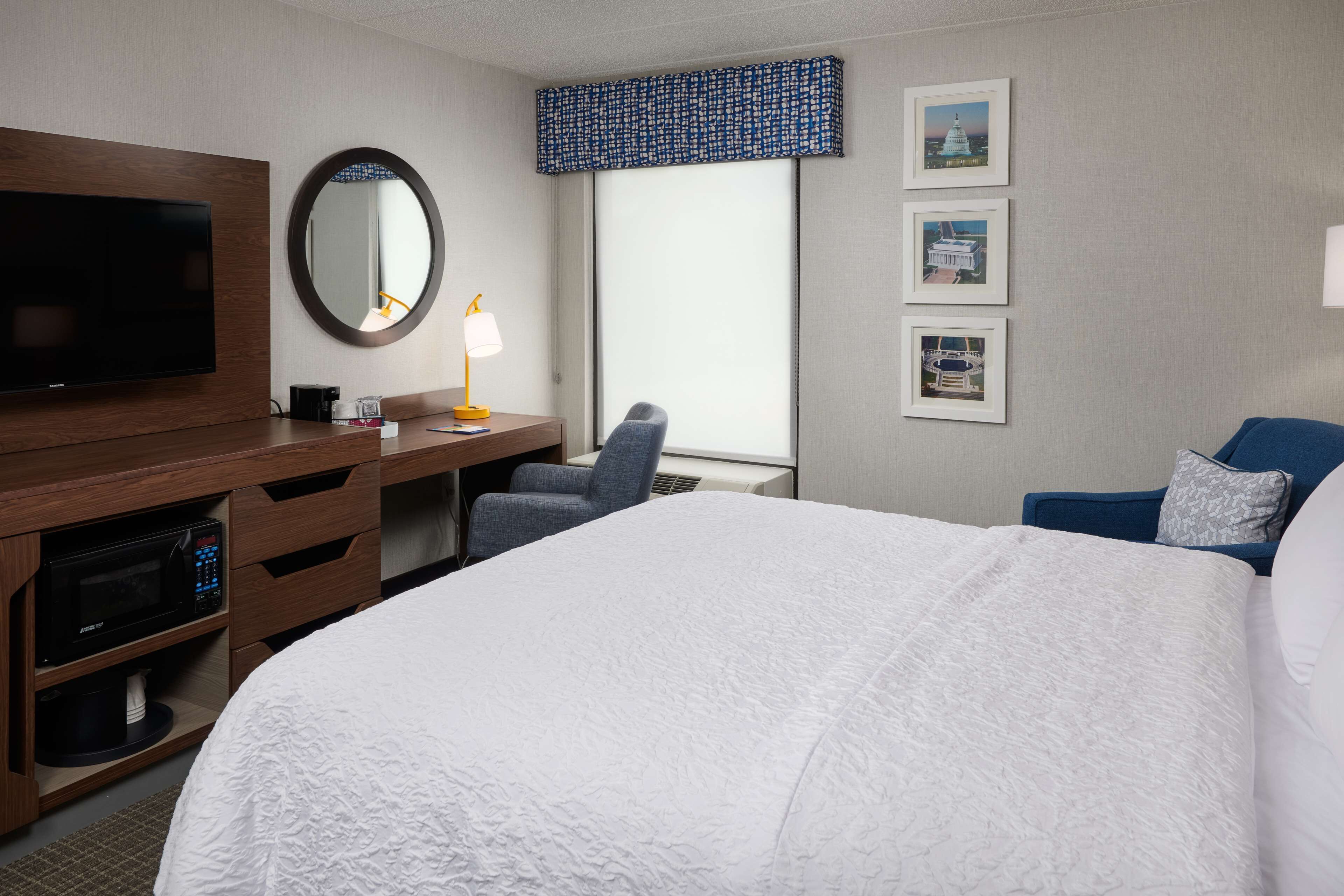 Une chambre d’hôtel avec un grand lit, un bureau équipé d’un ordinateur et d’une lampe, une télévision et une fenêtre donnant sur un immeuble.