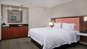 Habitación de hotel con una cama grande, un armario de madera, un espejo, una mesita de noche con lámpara y un teléfono.
