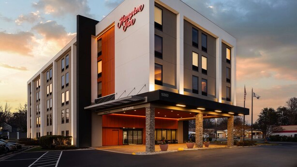 Un hotel moderno con un llamativo letrero de "Hampton Inn", una entrada acogedora y un estacionamiento.