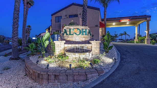 A building with a sign reading "ALOHA" surrounded by palm trees and a landscaped area with a water feature. - Aloha Inn (Arroyo Grande)