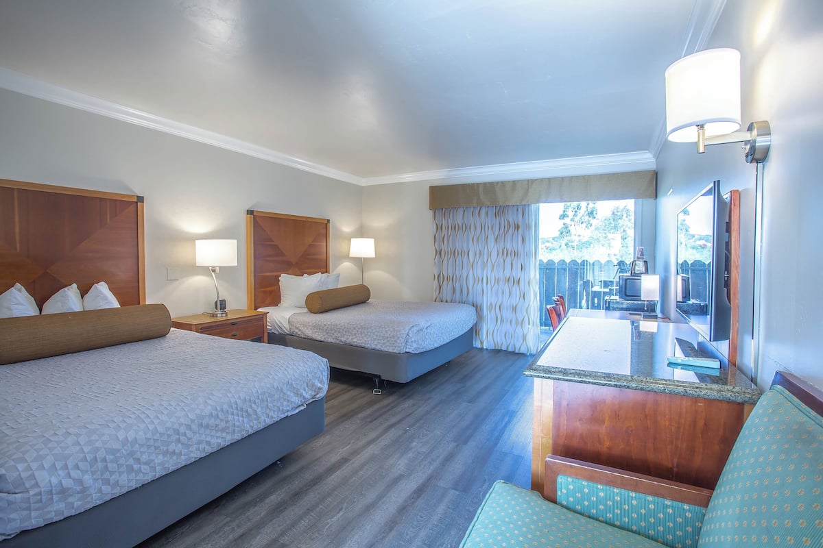 A hotel room with two beds, a desk, a chair, and a TV.