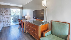 A hotel room with a wooden dresser, a television, a dining table with chairs, and a patterned curtain. - Aloha Inn (Arroyo Grande)