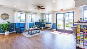 A hotel lobby with a blue wall, wooden flooring, a ceiling fan, a mirror, and a reception desk with informational brochures. - Aloha Inn (Arroyo Grande)
