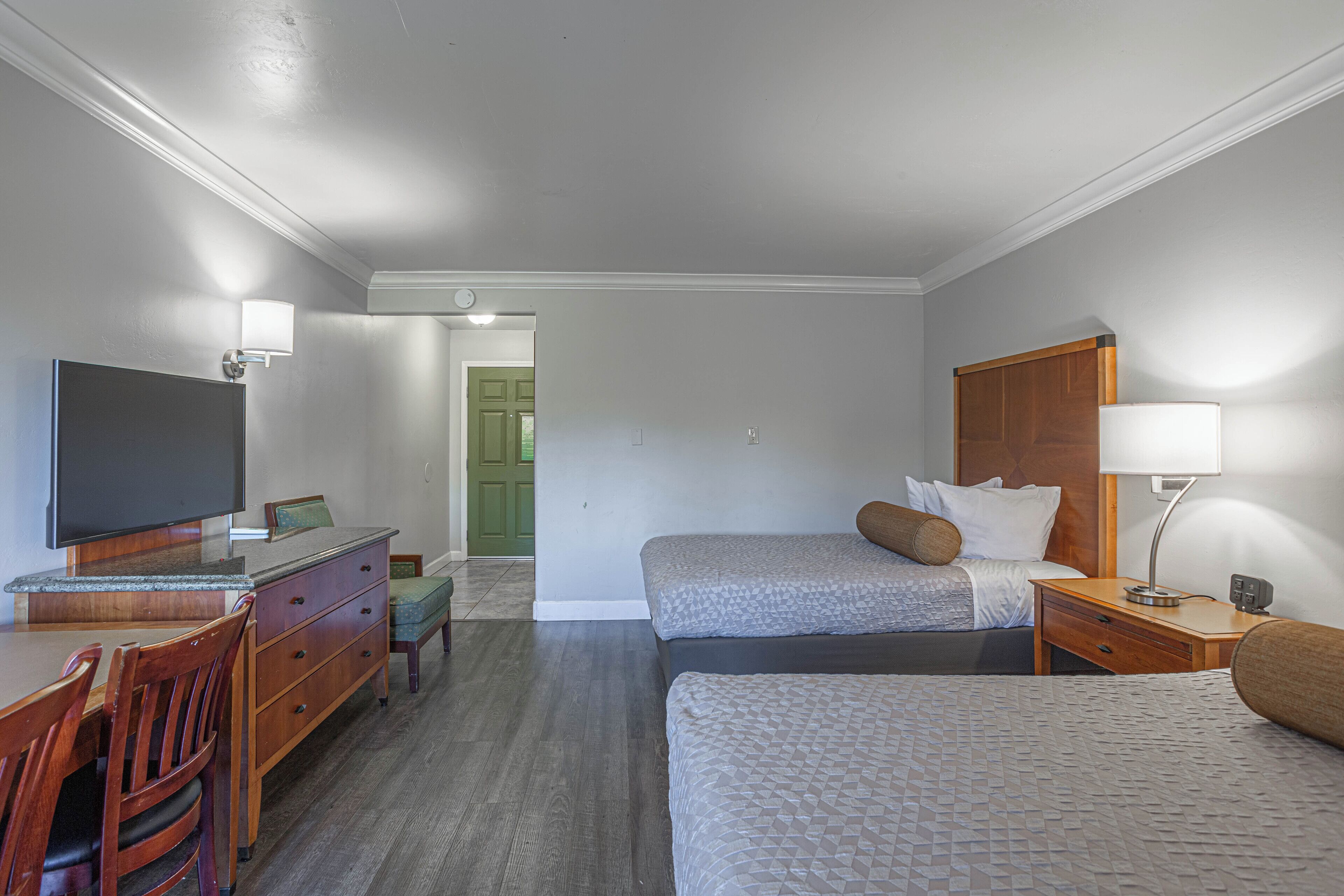 A hotel room with a bed, a desk with a television, a chair, and a lamp.