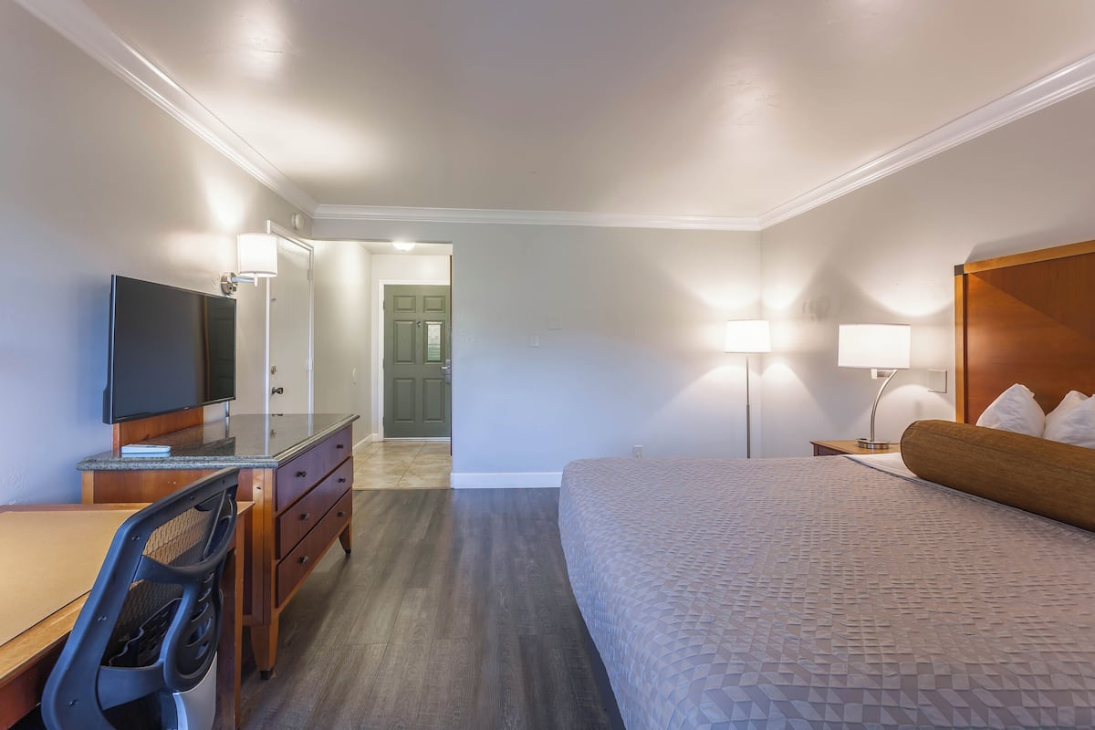A hotel room with a bed, desk, chair, television, and lamps.