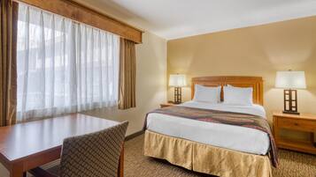 Camera d'albergo con un letto, due comodini con lampade, una scrivania con sedia e una finestra con tende.