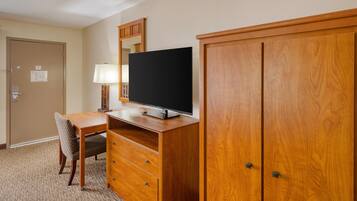 Ein Hotelzimmer mit Schreibtisch aus Holz, einem Fernseher, einem Sessel, einer Lampe und einem Kleiderschrank.