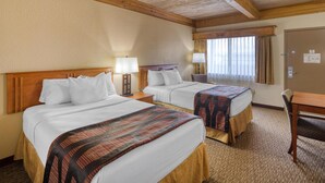 Habitación de hotel con dos camas, cabeceros de madera, una mesa de madera y un ventanal con cortinas.