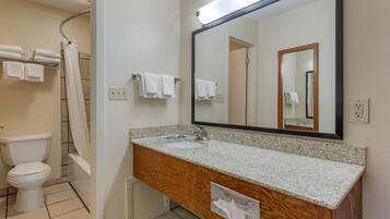 A bathroom with a white sink, wooden vanity, a large mirror, a shower curtain, and a toilet.