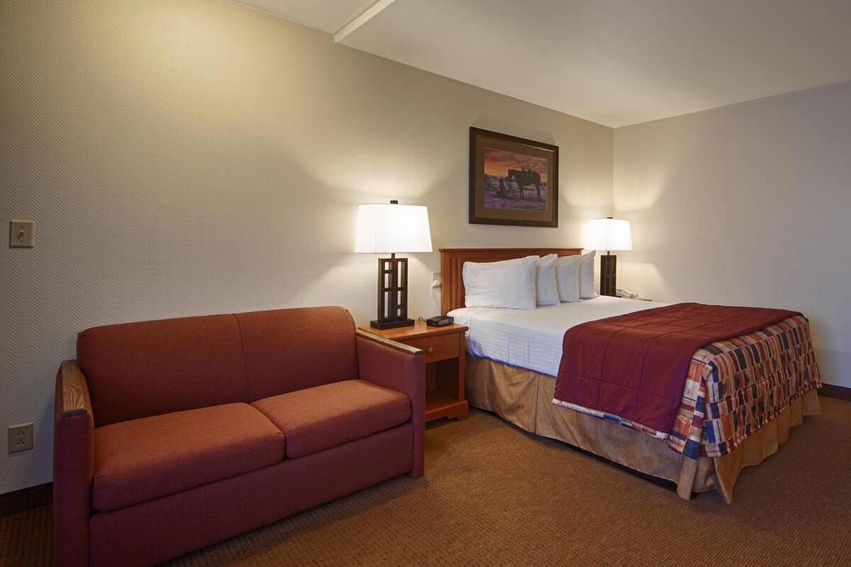 A hotel room with a bed, a sofa, two bedside lamps, a nightstand, and a painting on the wall.
