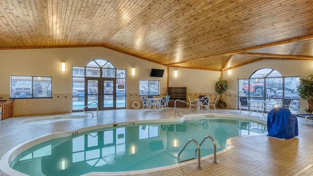 Una piscina interior con techo de madera, suelo de baldosas y ventanas grandes.
