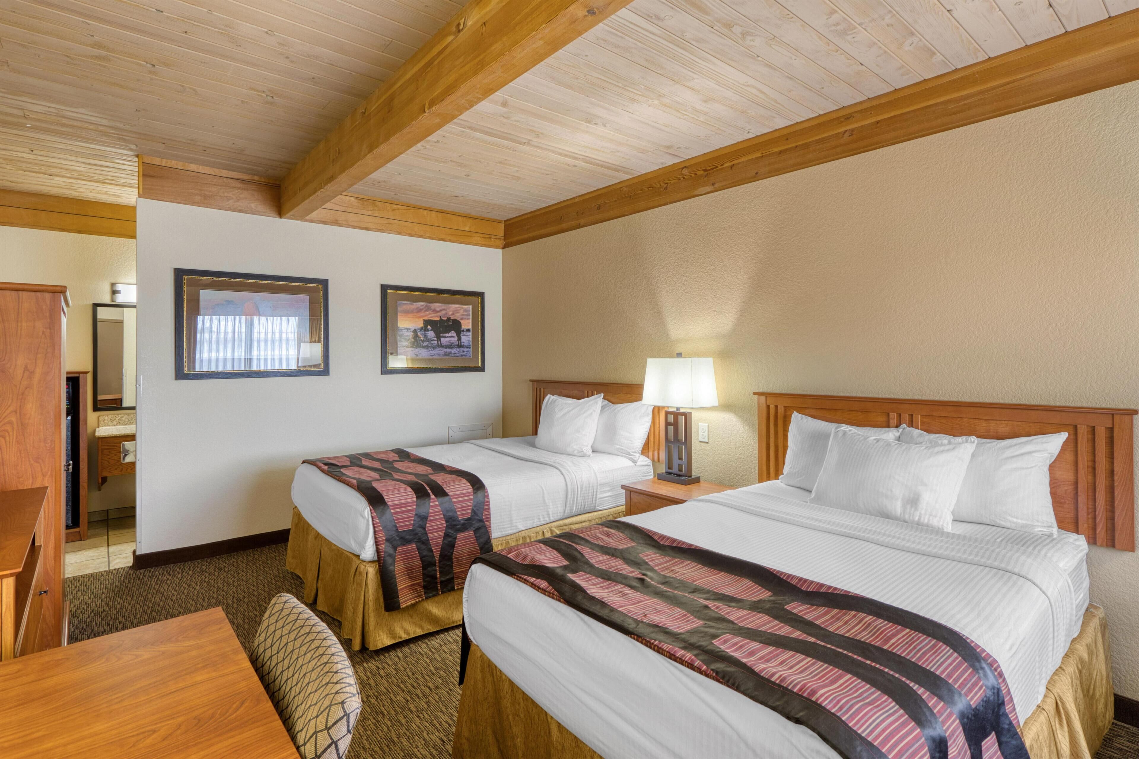 A hotel room with two beds, wooden headboards, a desk, and a chair.