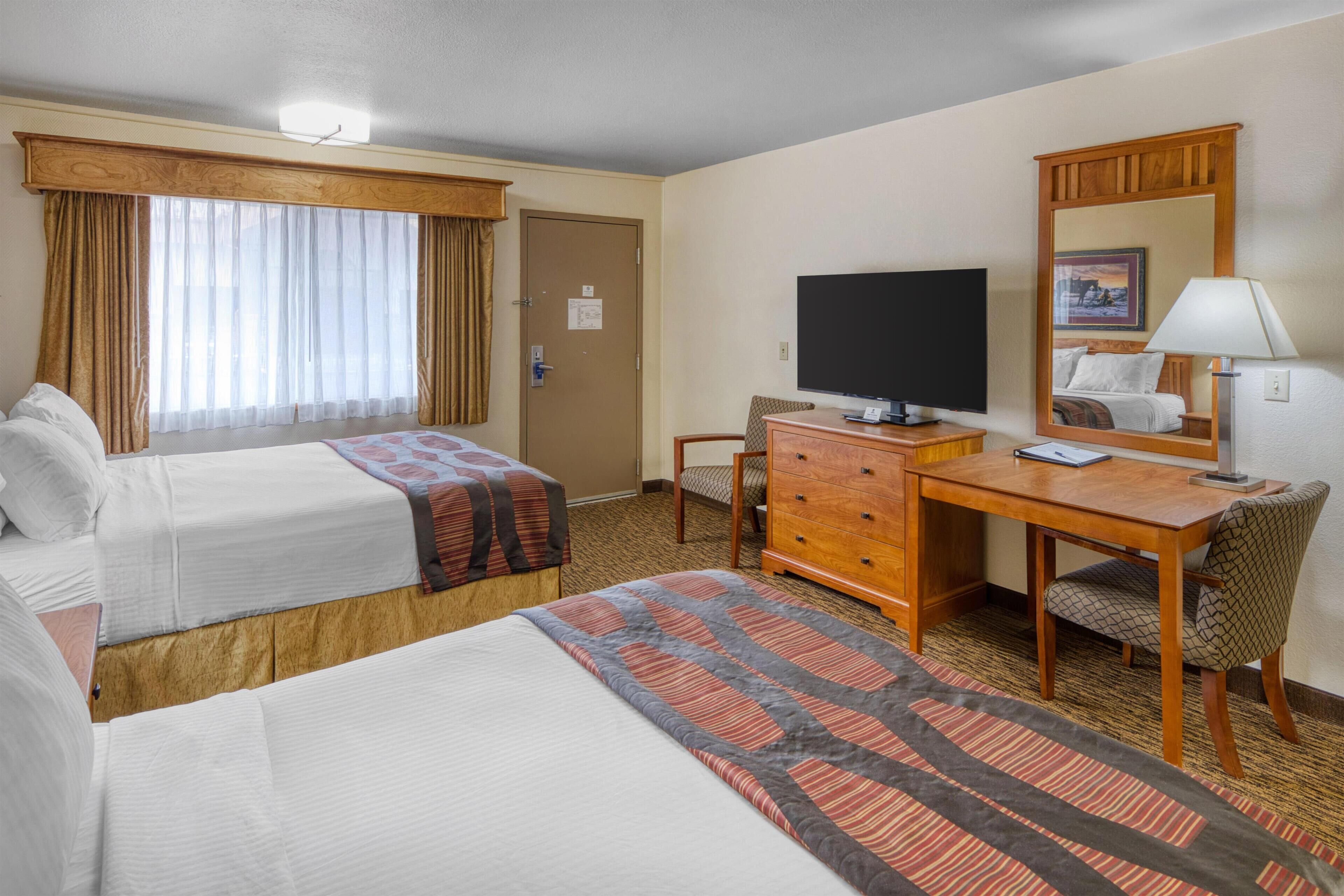 A hotel room with two beds, a desk with a computer, a chair, a TV, and a mirror.
