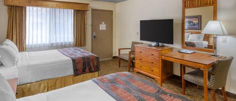 Habitación de hotel con dos camas, un escritorio con computadora, una silla, un televisor y un espejo.