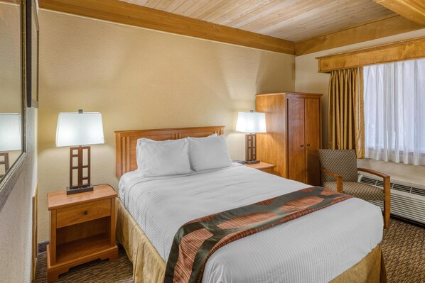 A hotel room with a bed, two bedside lamps, a wooden nightstand, a wardrobe, a chair, and a window with curtains.