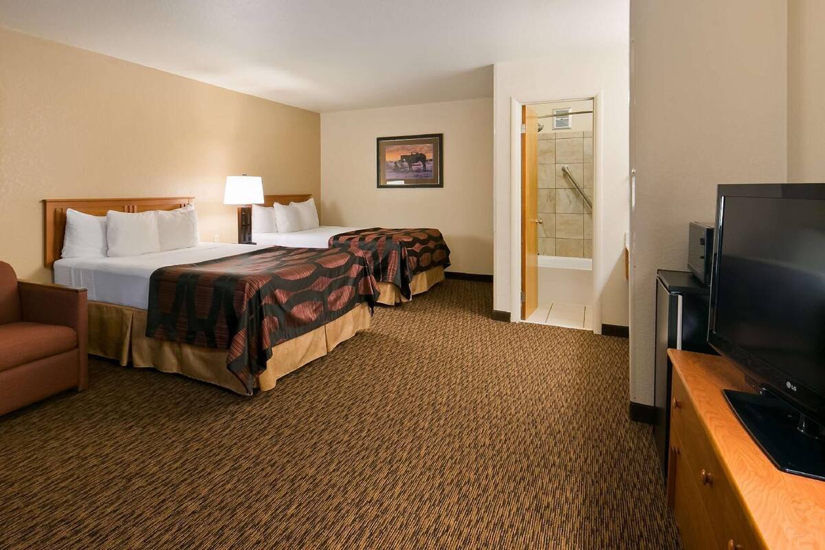 A hotel room with a bed, two bedside tables, a TV, a couch, and a carpeted floor.
