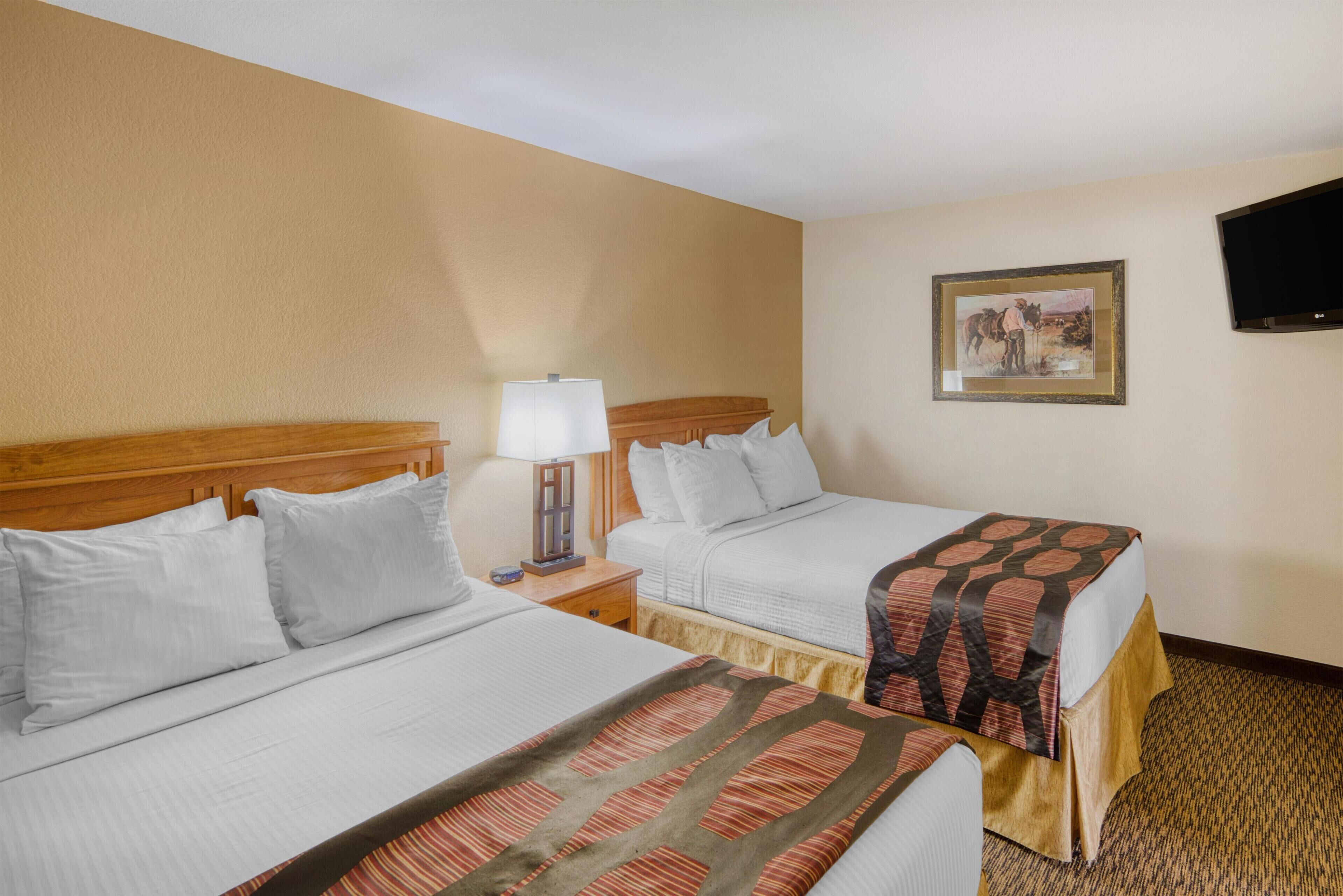 Two single beds with white linens, a wooden headboard, a bedside table with a lamp, and a framed picture on the wall.