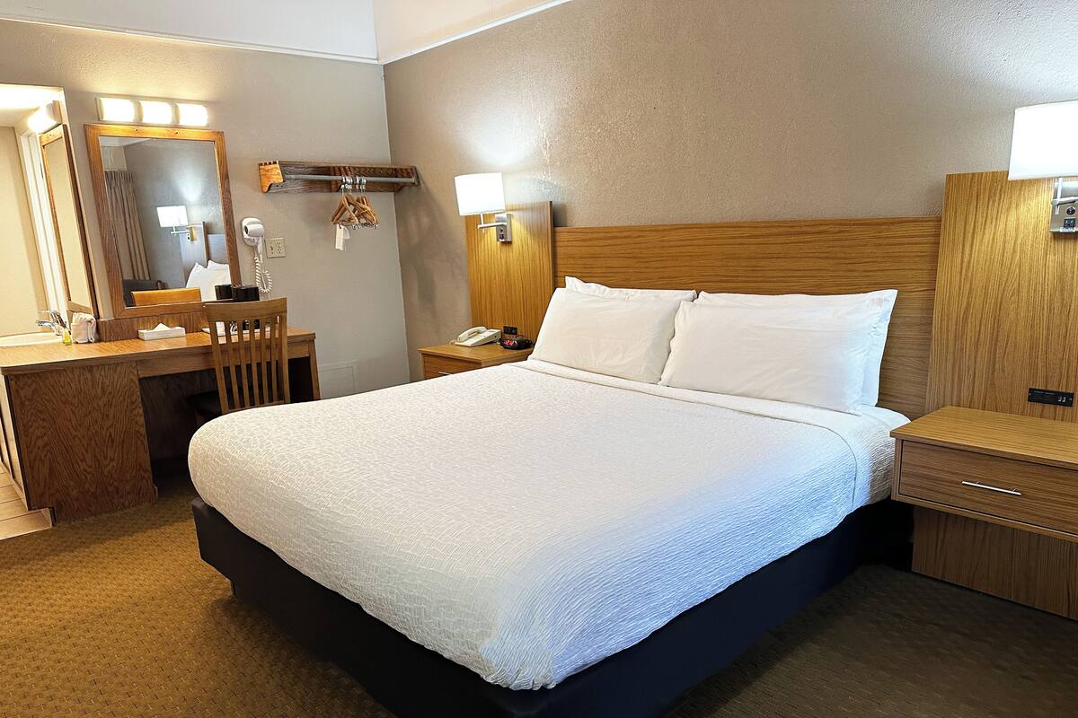 Une chambre d’hôtel avec un grand lit, un bureau en bois, un miroir, une table de chevet et une lampe fixée au mur.