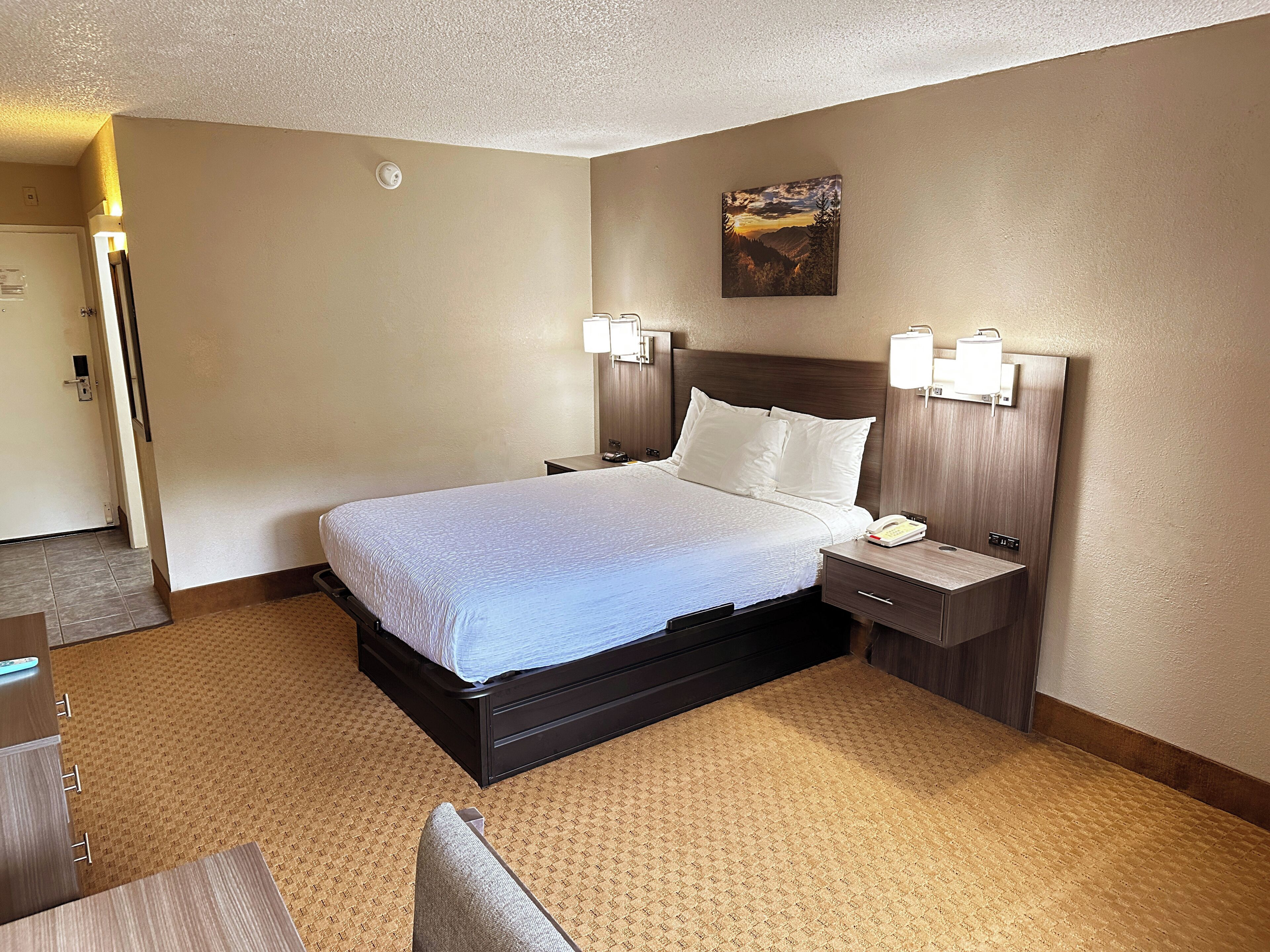 Une chambre d’hôtel avec un grand lit, des tables de chevet, une commode, un tableau au mur et une porte.