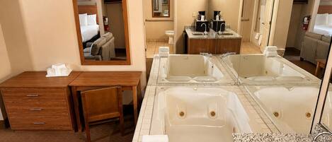 A hotel bathroom with a large bathtub, a sink, and a mirror.