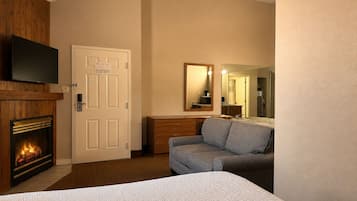 A hotel room with a fireplace, a television mounted above it, a sofa, a bed, and a mirror reflecting the room.