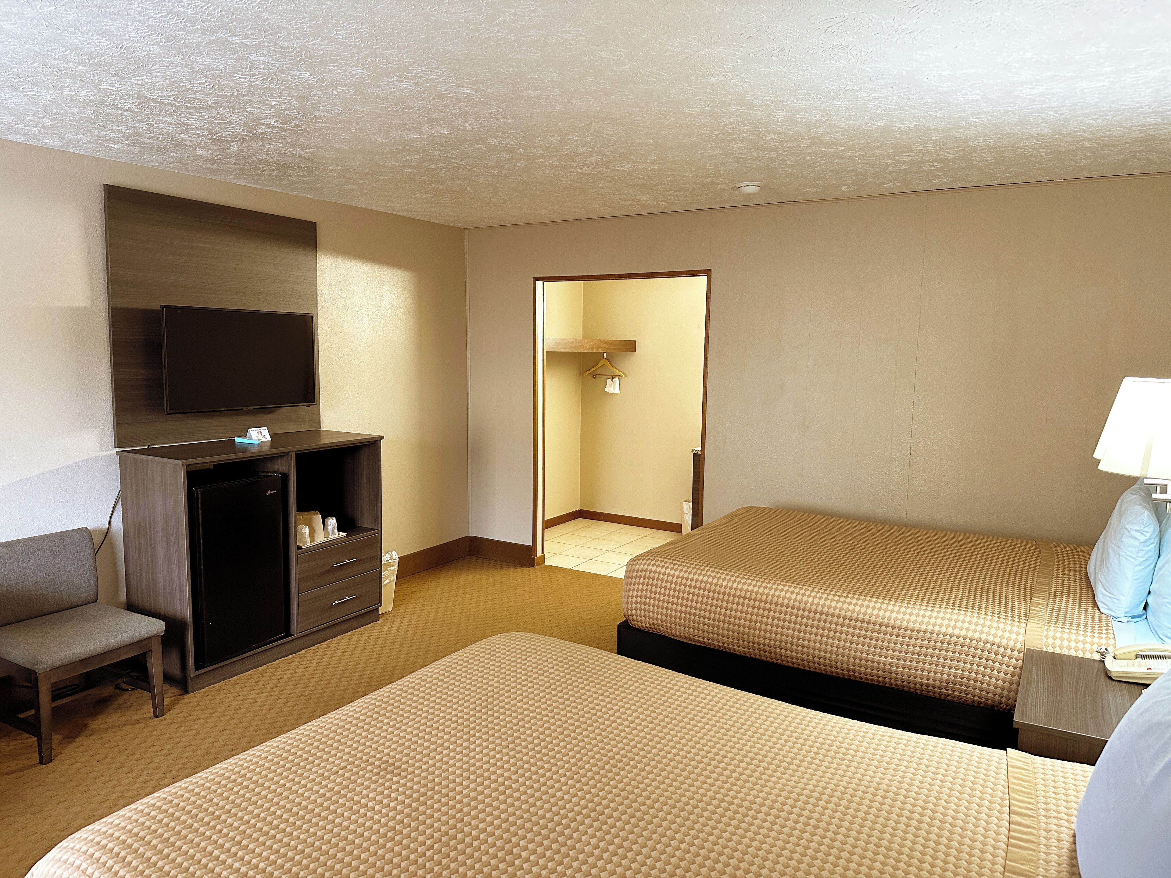 Habitación de hotel con dos camas, un escritorio, un televisor y una pequeña kitchenette.