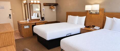 A hotel room with two beds, a desk, a mirror, and a bedside table with lamps.