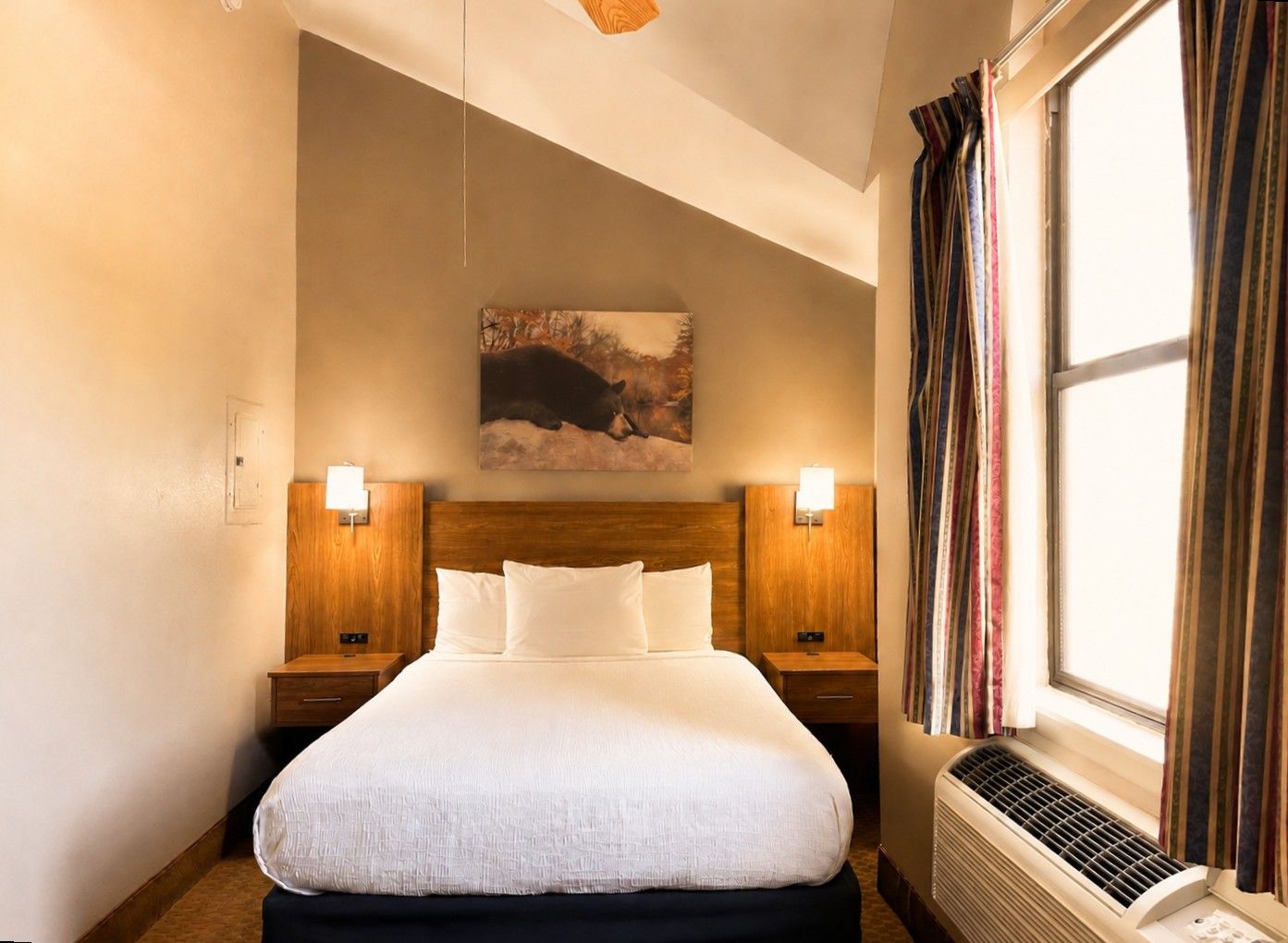 Ein Hotelzimmer mit einem großen Bett, zwei Nachttischen, einem Wandbild, einem Fenster mit Vorhängen und einem Wandheizgerät.