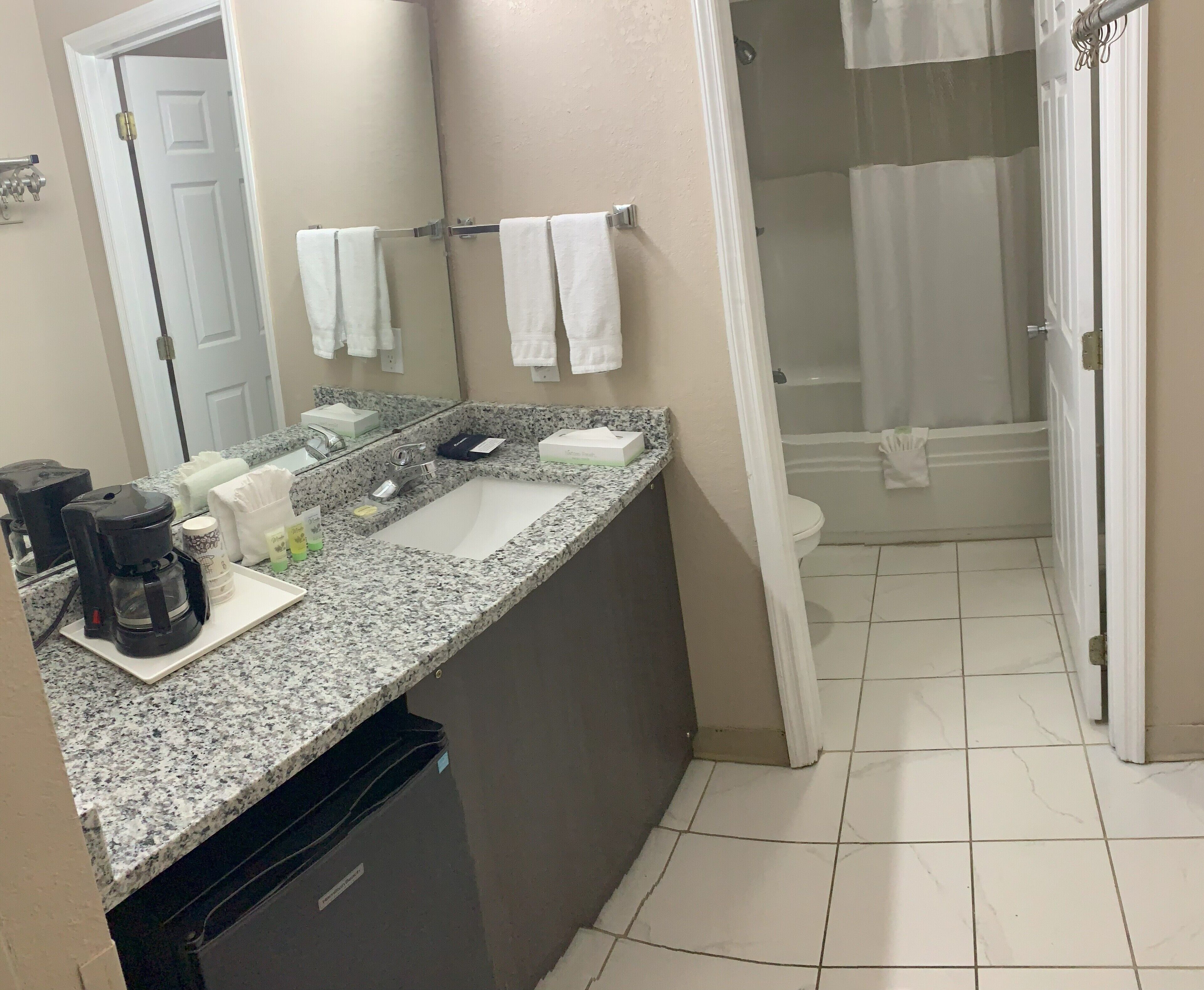 A bathroom with a granite countertop, a coffee maker, a sink, and a shower area.