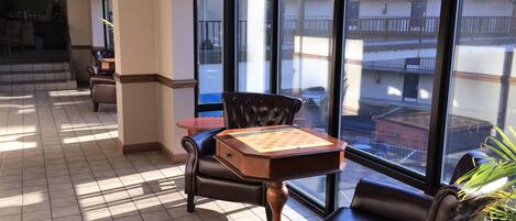 A hotel room with a large window, a chess table, leather chairs, and a small table.