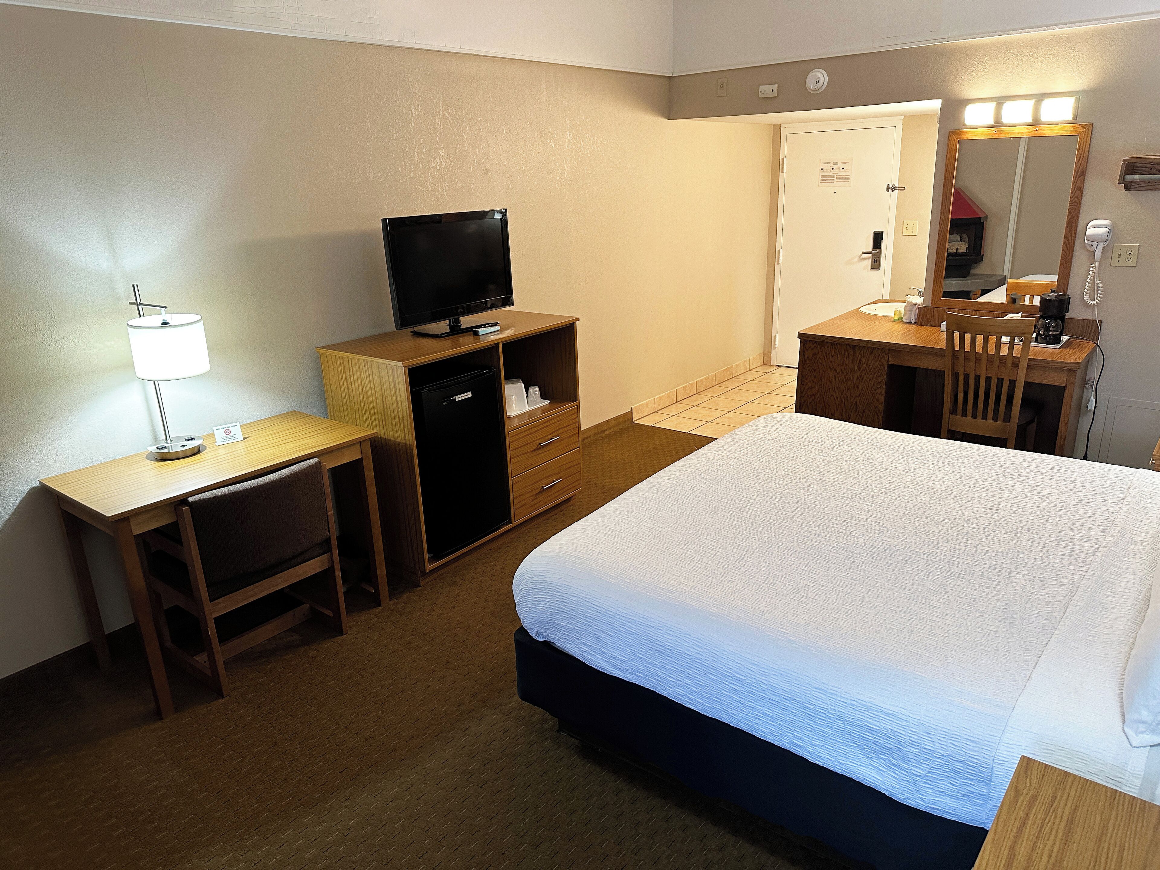 Een hotelkamer met een bed, een bureau met lamp, een televisie, een dressoir en een spiegel.