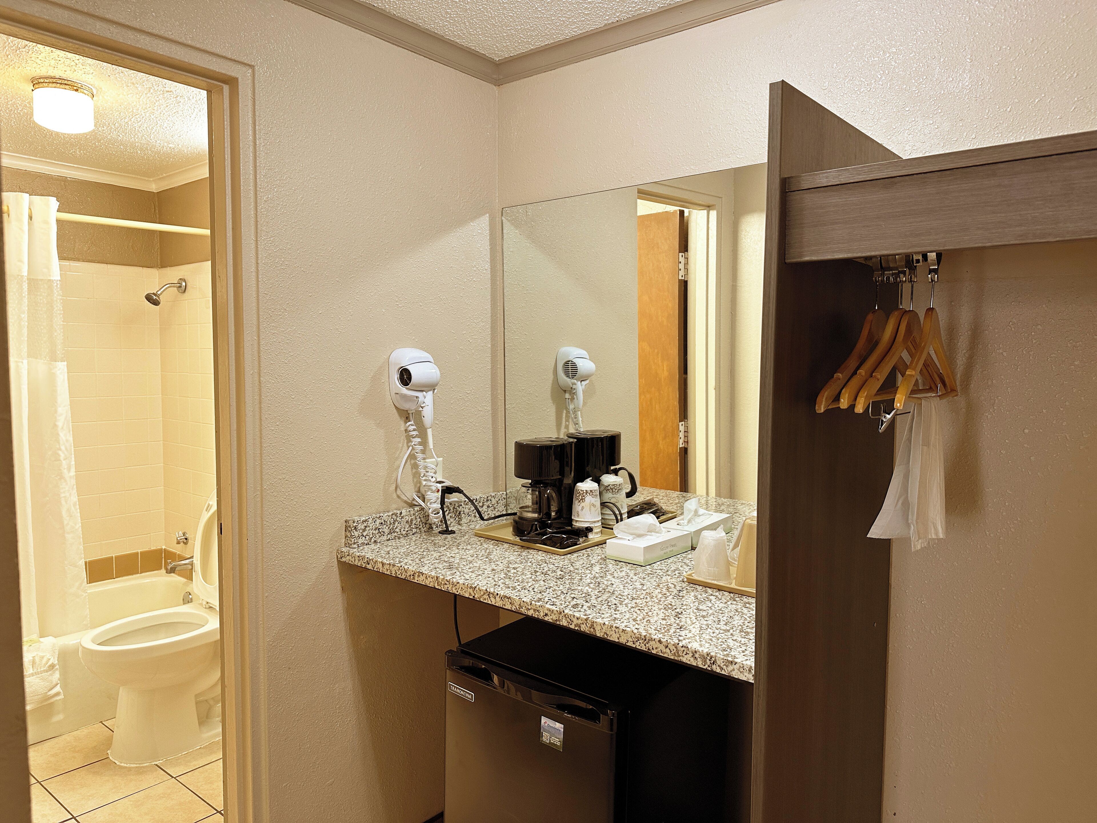A bathroom with a shower, toilet, and a sink with a mirror. There are hair dryers and a coffee maker on the counter.