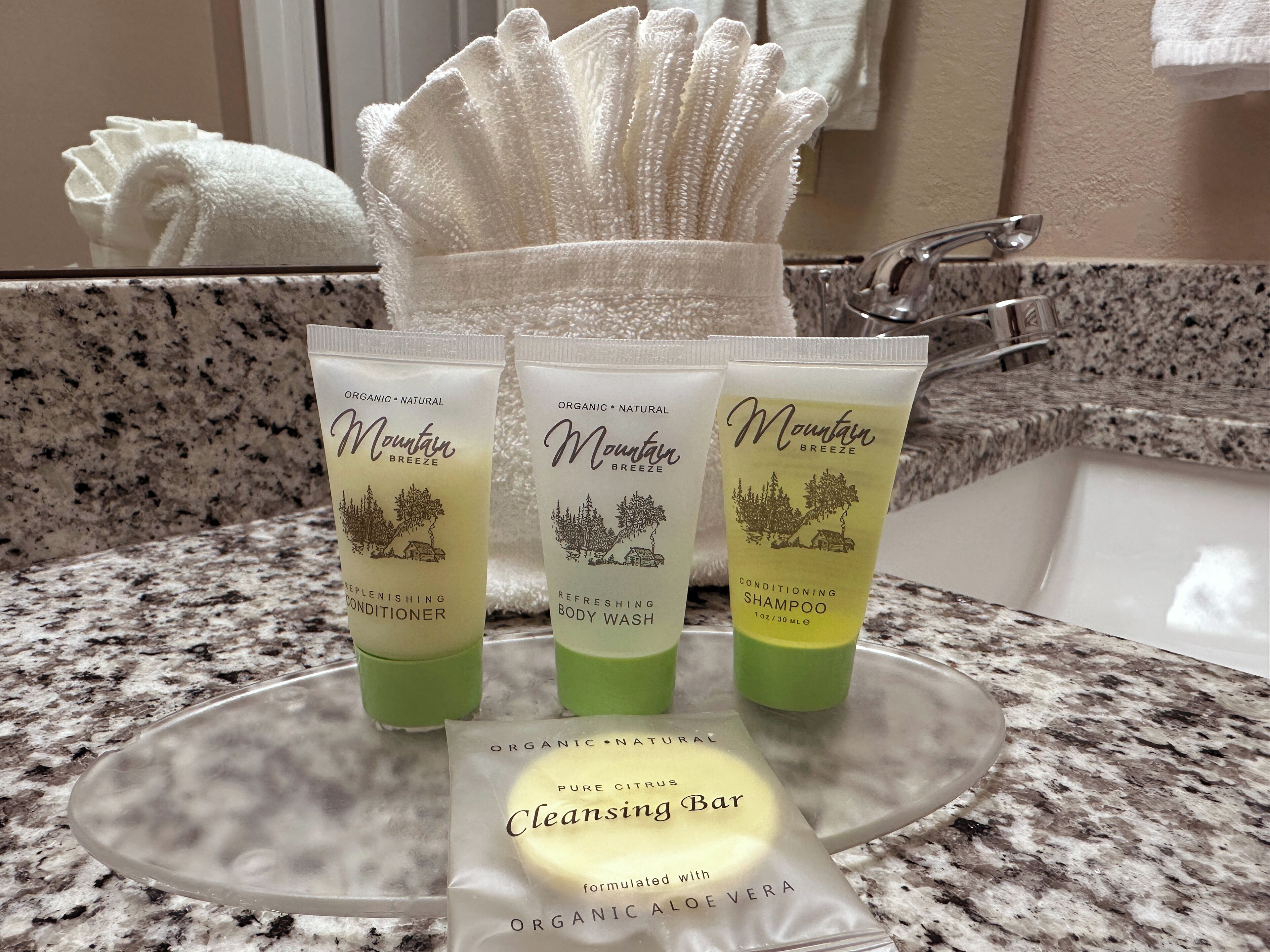 Drei Flaschen Mountain Breeze Duschgel und eine Stange Pure Citrus Reinigungseife auf einer Granitarbeitsplatte.