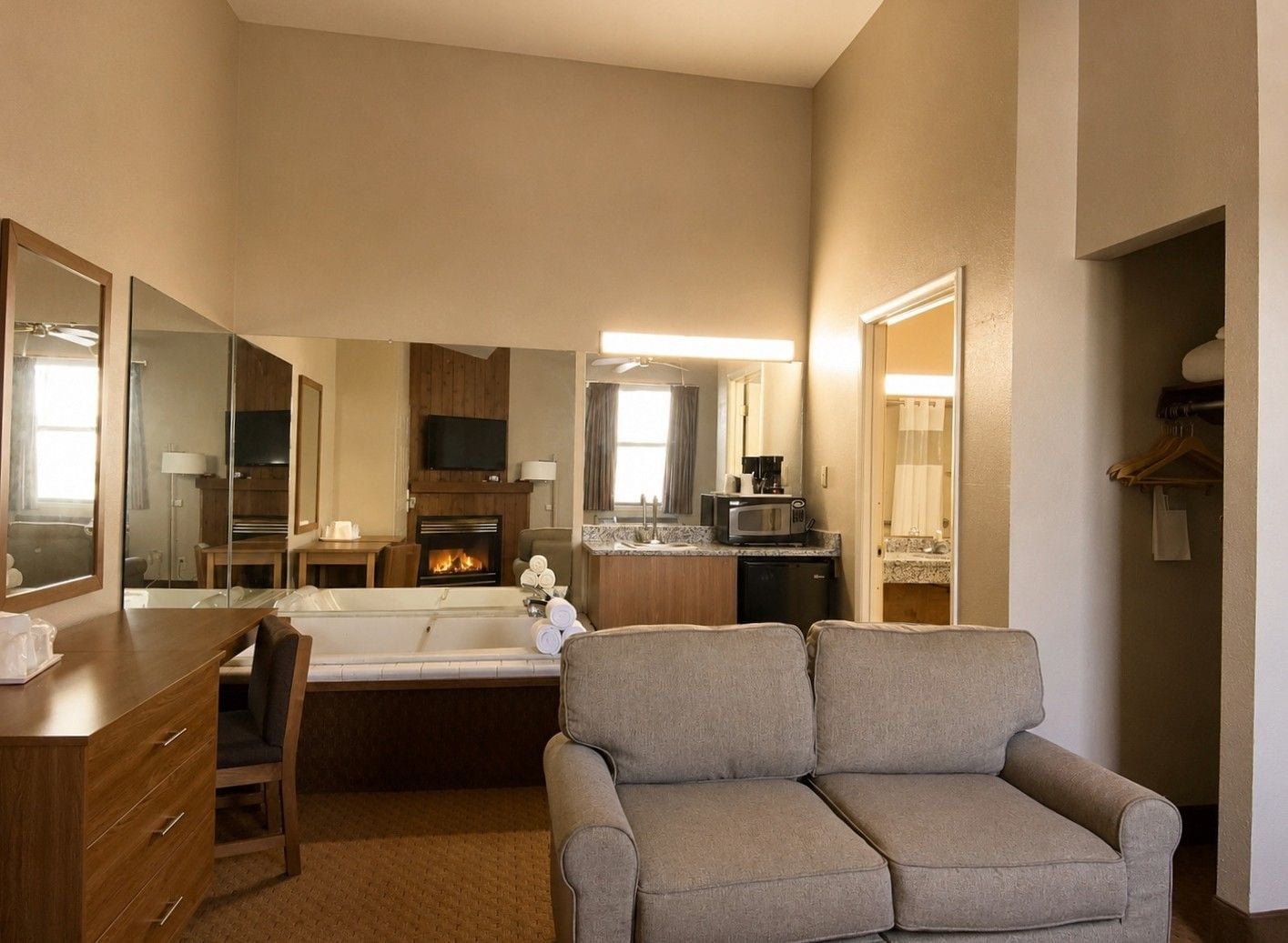 A hotel room with a sofa, a small table, a TV, a fireplace, a microwave, and a bathroom visible through an open door.