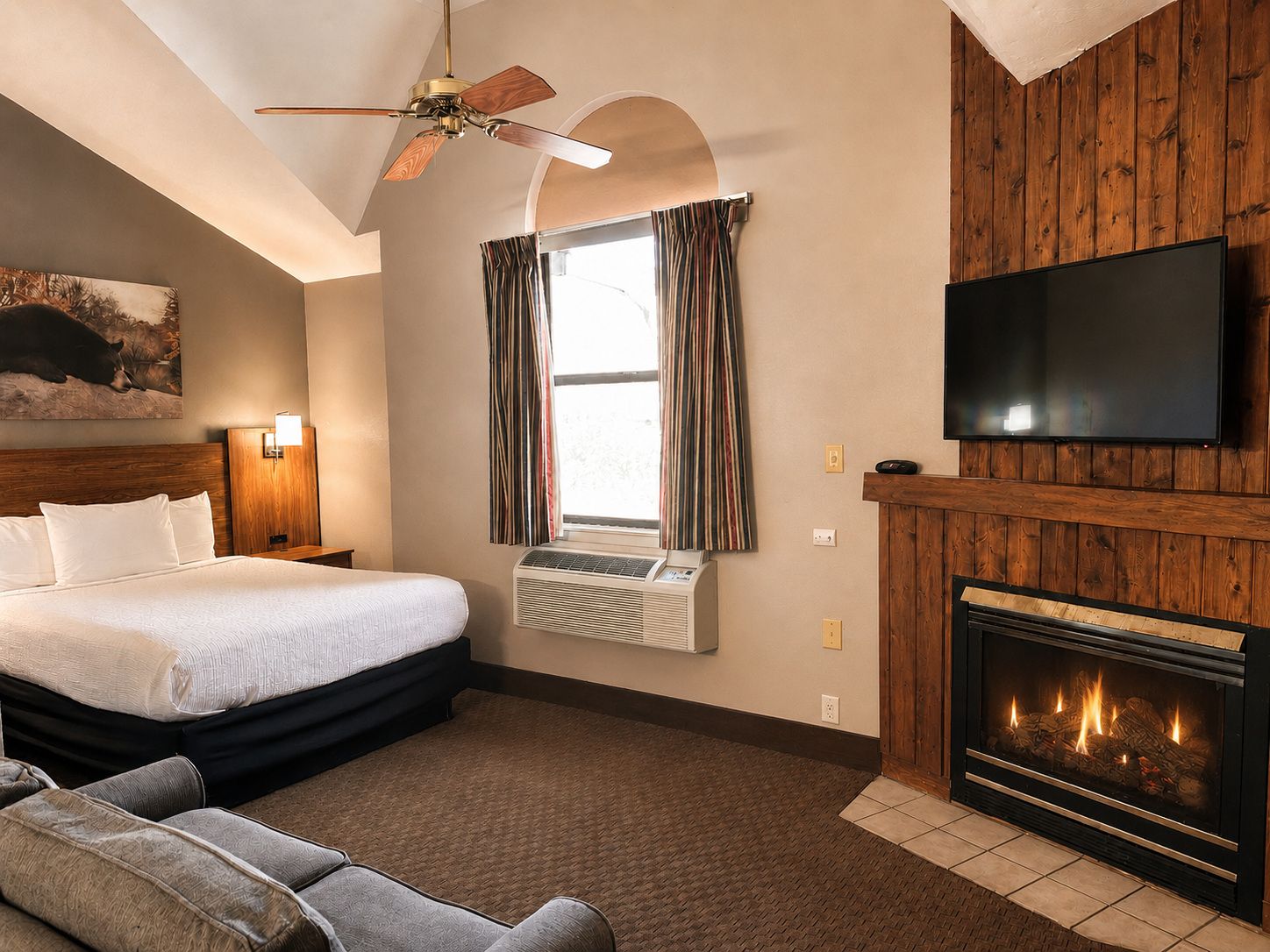 A hotel room with a bed, a television, a fireplace, and a ceiling fan.