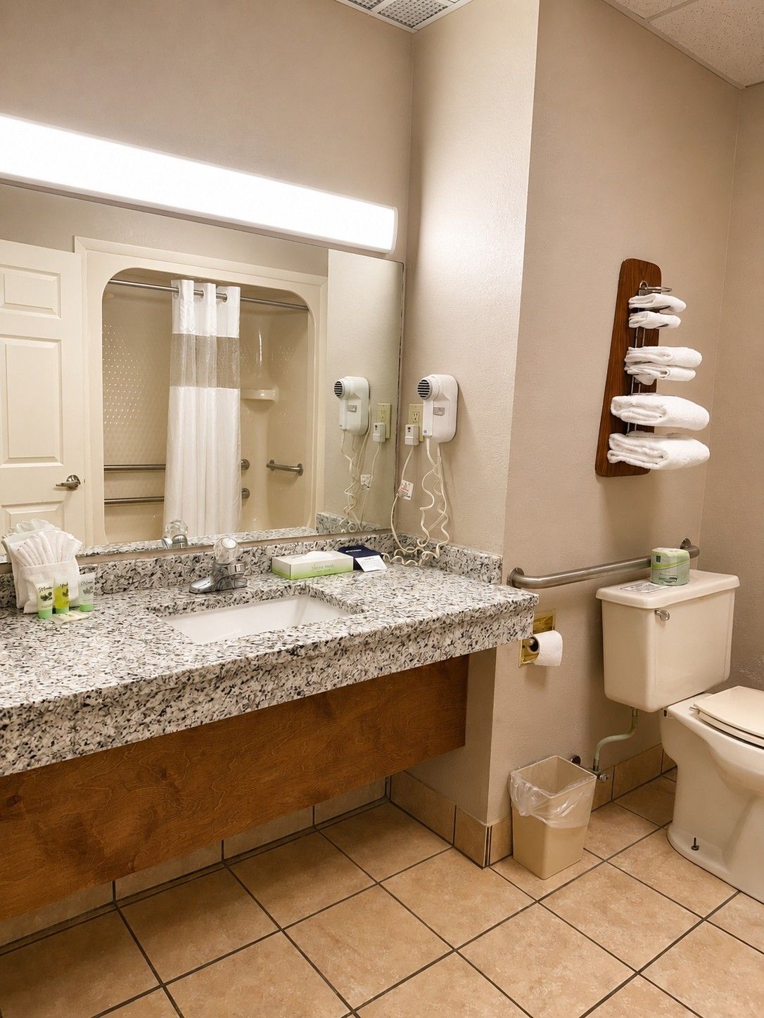 A bathroom with a granite countertop, a toilet, a hand dryer, a towel rack, and a mirror.
