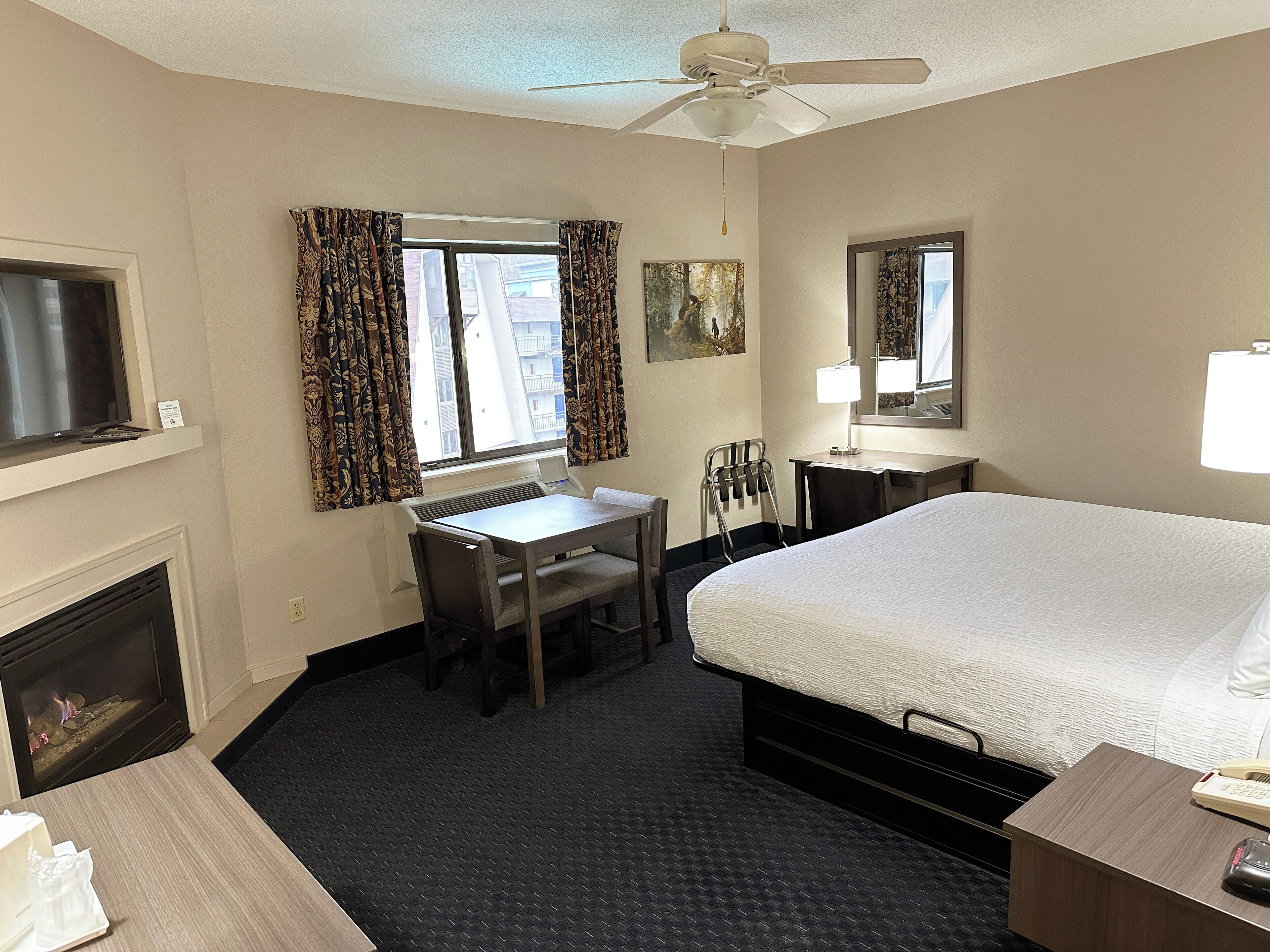 Habitación de hotel con cama, escritorio, silla, televisor, chimenea y ventana con cortinas.