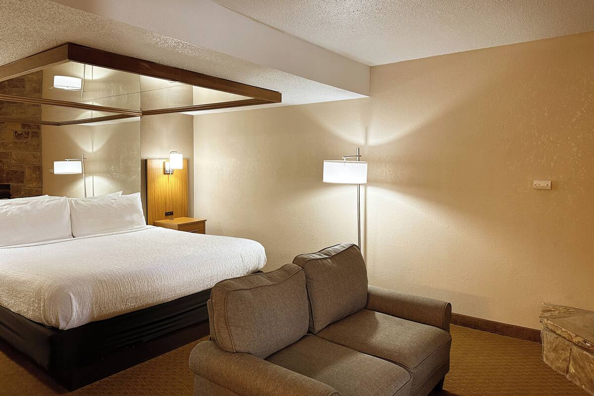 Une chambre d’hôtel avec un grand lit, un canapé, une table de chevet et une lampe fixée au mur.