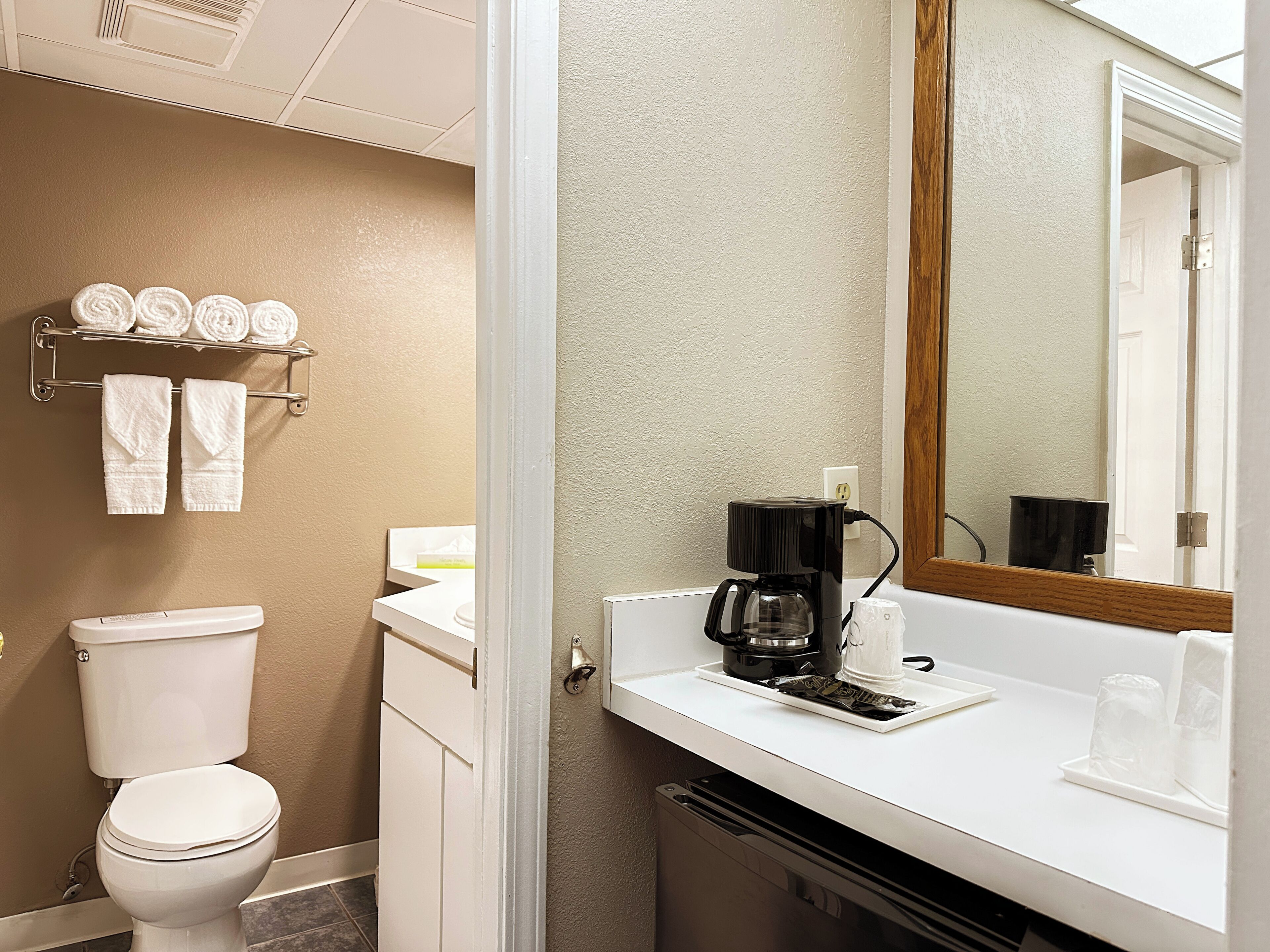 A bathroom with a toilet, a sink with a coffee maker, and a towel rack with towels.