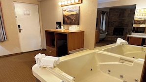 Una habitación de hotel con una bañera grande, un armario de madera, un refrigerador y una chimenea de piedra.