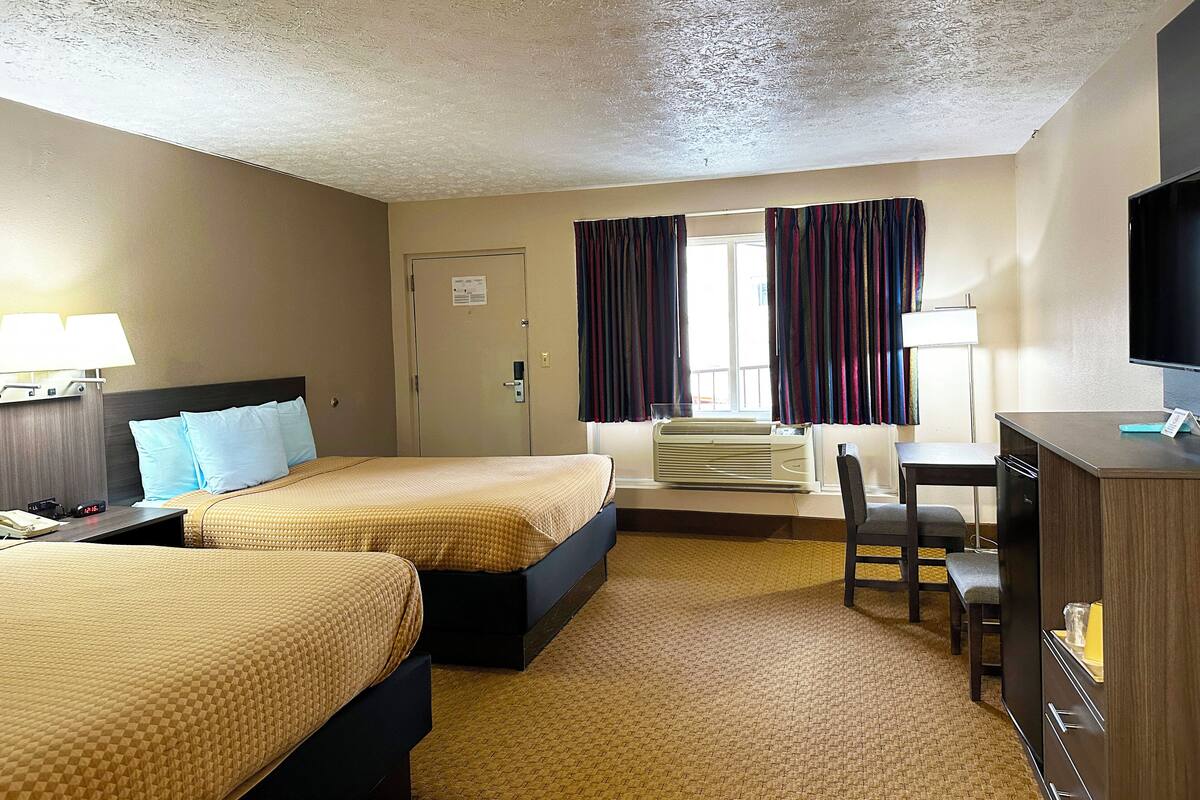 Une chambre d’hôtel avec deux lits, un bureau, une chaise, une télévision et une fenêtre avec des rideaux.