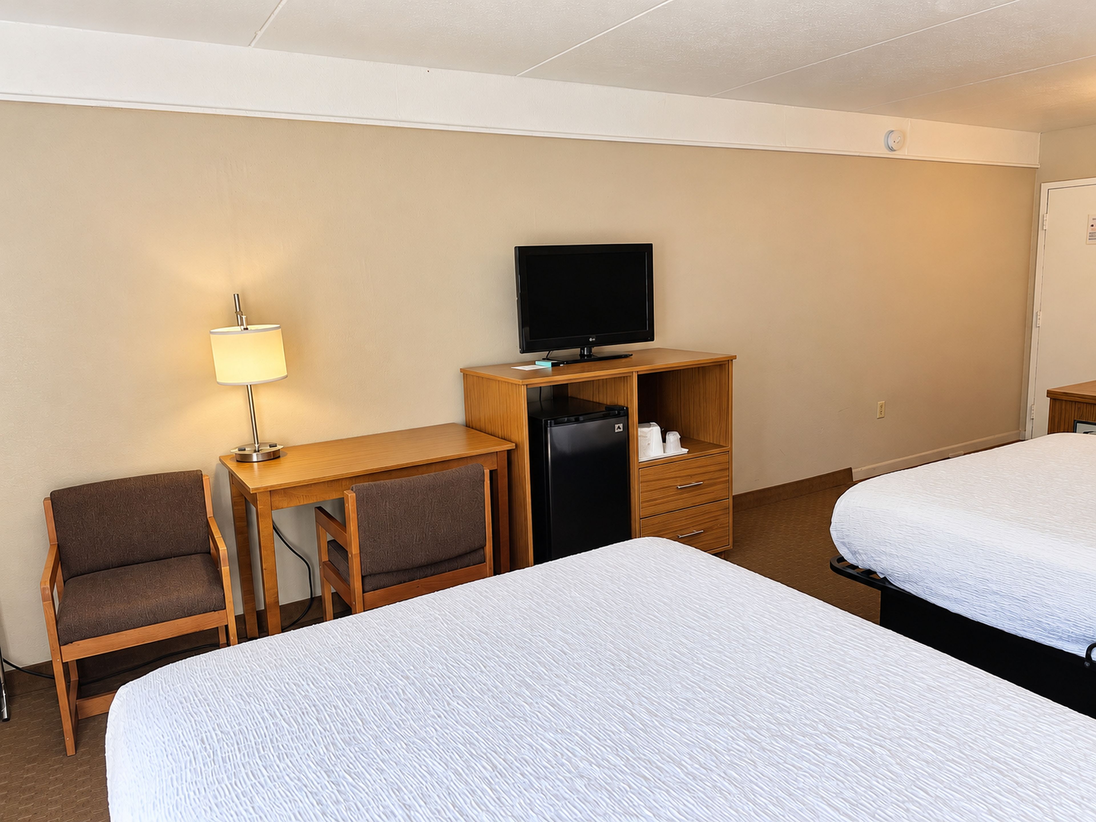 Ett hotellrum med två sängar, ett skrivbord med en tv, en stol och en lampa.