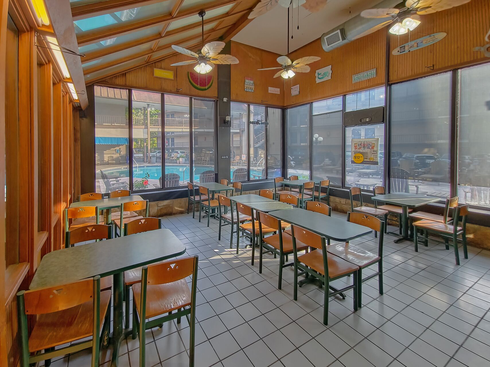 A restaurant with wooden walls, large windows, and ceiling fans. Tables and chairs are arranged for dining.