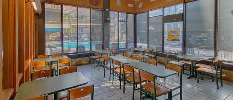 A restaurant with wooden walls, large windows, and ceiling fans. Tables and chairs are arranged for dining.