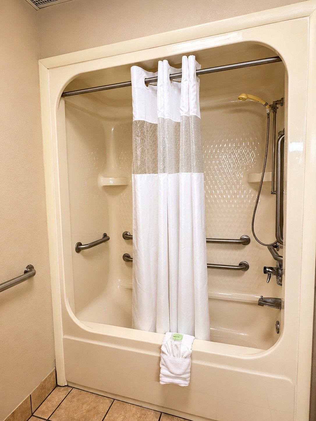 A bathtub with a shower curtain, grab bars, and a handheld showerhead.